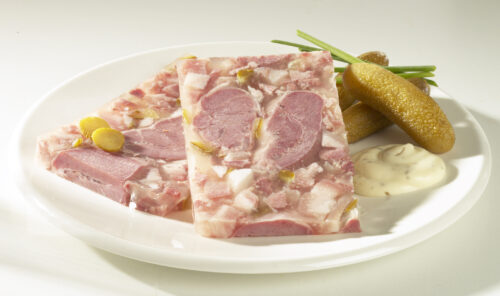 ein Teller mit zwei Scheiben Spreewälder Gurkensülze, zur Deko anbei Spreewälder Gurken am rechten Tellerrand